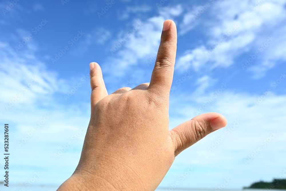 woman hand and fingers gesturing sign i love you on blue sky background woman hand and fingers gesturing sign i love you on blue sky background