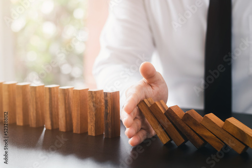 Risk management, business man hand Stop the continuous falling of wooden dominoes, stop the impact of the business crisis. hedging Solving business problems for success.