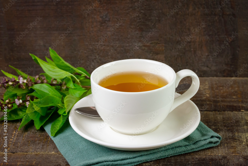 Basil tea in white cup ceramic with green leaf on rustic wooden table. Basil is food and herb for healthy. Basil tea in white cup ceramic with green leaf on rustic wooden table. Basil is food and herb for healthy.