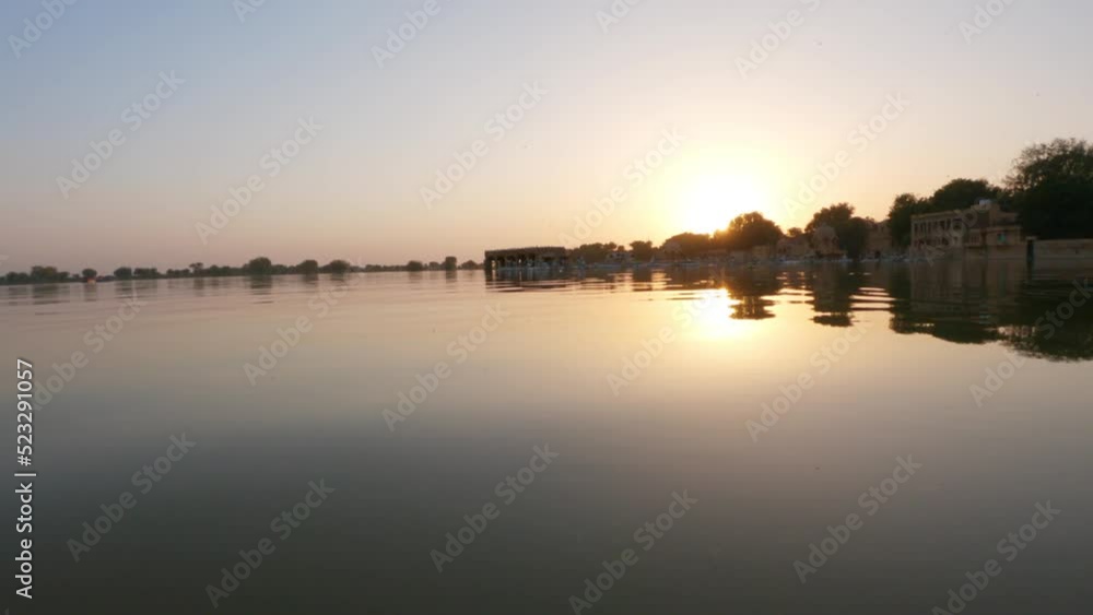 4K View of the Gadisar Lake during sunset with chhatri in the middle of the lake at Jaisalmer in Rajasthan, India. Reflection of the Chhatri pavilion in the orange water of the lake during sunset. 4K View of the Gadisar Lake during sunset with chhatri in the middle of the lake at Jaisalmer in Rajasthan, India. Reflection of the Chhatri pavilion in the orange water of the lake during sunset.