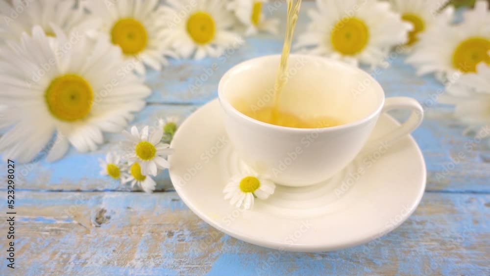 Composition with chamomile flowers and white cup of herbal tea on vintage light blue wooden table top. Summer theme. Composition with chamomile flowers and white cup of herbal tea on vintage light blue wooden table top. Summer theme.