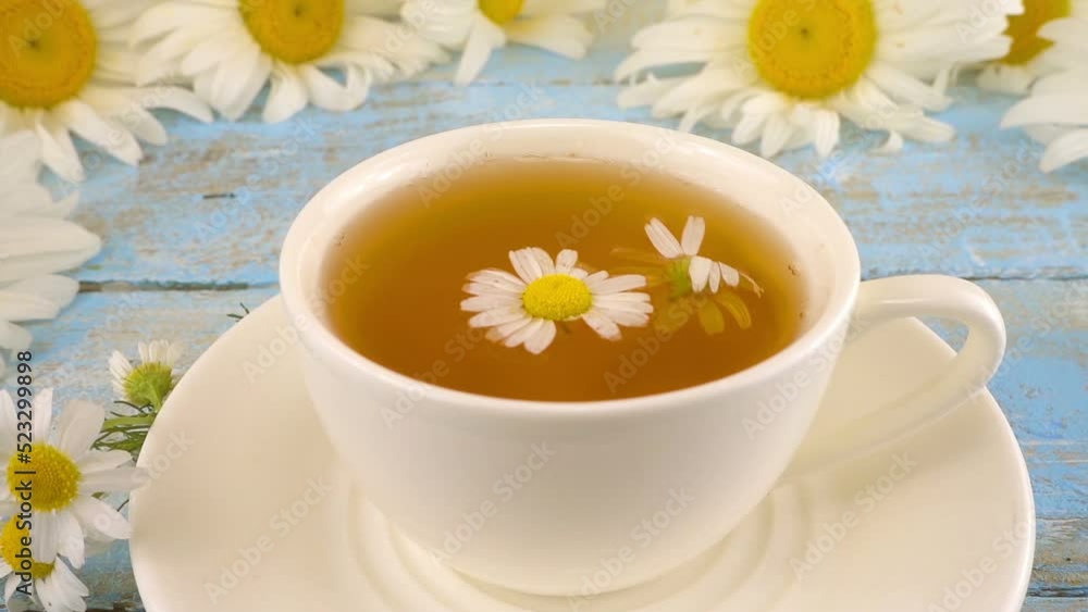 Composition with chamomile flowers and white cup of herbal tea on vintage light blue wooden table top. Summer theme. Composition with chamomile flowers and white cup of herbal tea on vintage light blue wooden table top. Summer theme.