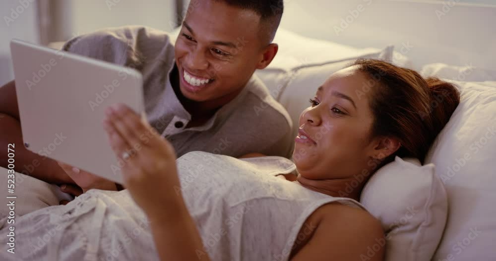 Laughing, cozy couple bonding and browsing on a digital tablet in bed, watching an online video. Happy husband and wife searching for something to watch and keep them entertained at home Laughing, cozy couple bonding and browsing on a digital tablet in bed, watching an online video. Happy husband and wife searching for something to watch and keep them entertained at home