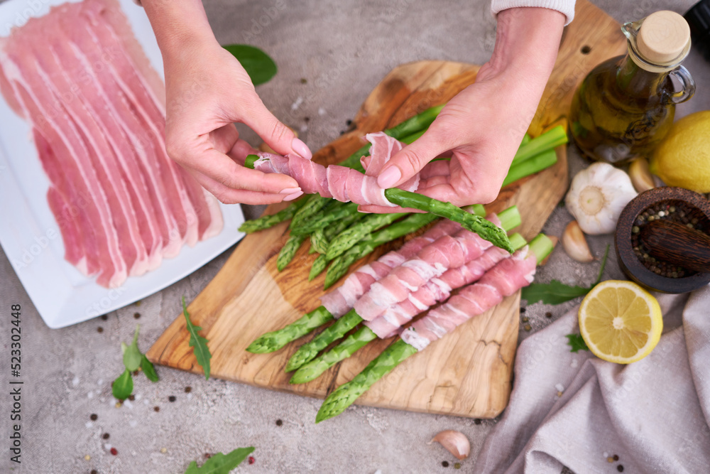 woman cooking green aspargus covered with bacon at domestic kitchen