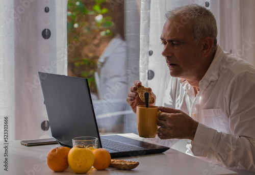 man having breakfast while working with his laptop