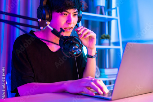 Playing video games on smartphone. Young asian handsome man sitting on chair holding cellphone in his hand. Exited streamer wearing headset in neon room .Esport streaming game online.