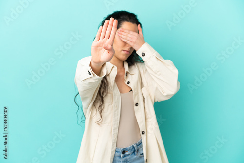 Young caucasian woman isolated on blue background making stop gesture and covering face