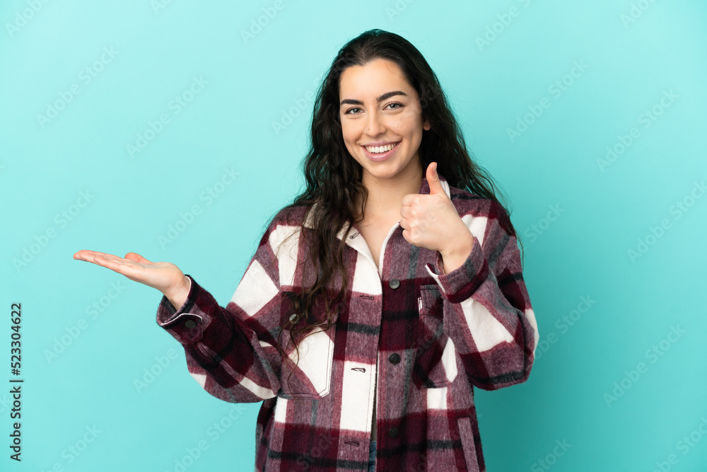 Young caucasian woman isolated on blue background holding copyspace imaginary on the palm to insert an ad and with thumbs up Young caucasian woman isolated on blue background holding copyspace imaginary on the palm to insert an ad and with thumbs up