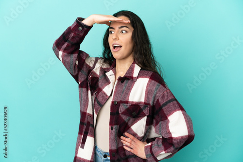 Young caucasian woman isolated on blue background doing surprise gesture while looking to the side