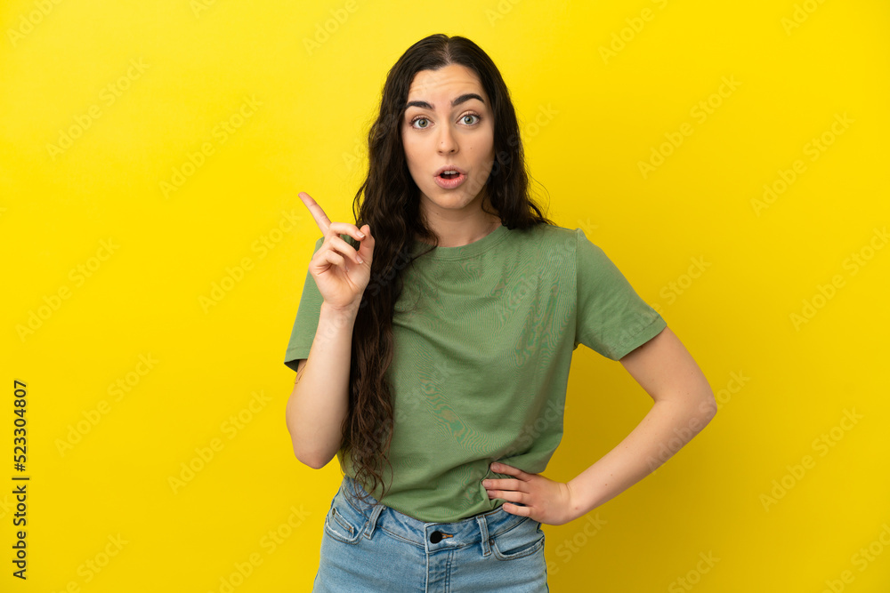 Young caucasian woman isolated on yellow background intending to realizes the solution while lifting a finger up Young caucasian woman isolated on yellow background intending to realizes the solution while lifting a finger up