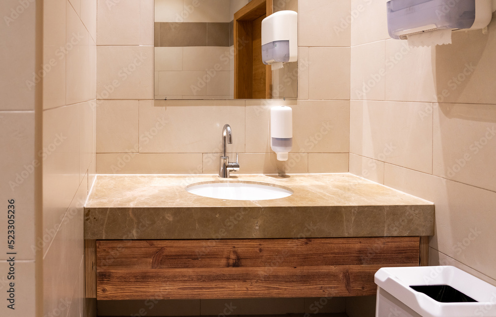 Sink in modern public toilet with paper towels and wastebasket Sink in modern public toilet with paper towels and wastebasket