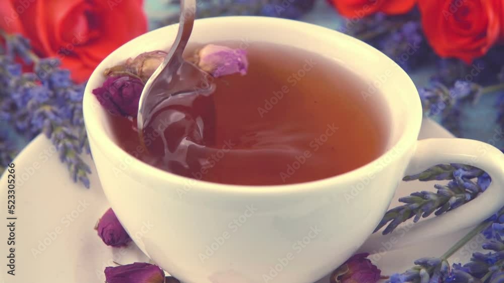Provencal style composition: tea with fragrant rose buds, fresh rose flowers and lavender on a vintage light blue wooden tabletop. Slow motion. Provencal style composition: tea with fragrant rose buds, fresh rose flowers and lavender on a vintage light blue wooden tabletop. Slow motion.