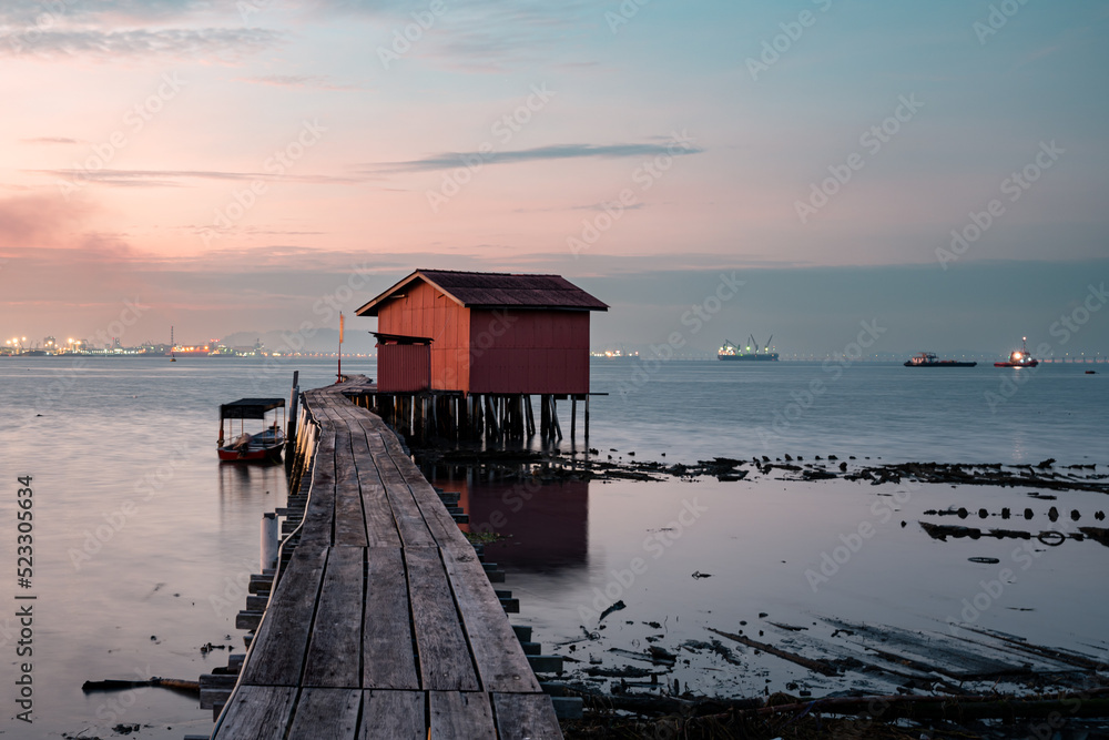 Sunrise view of wooden bridge and red house background at Clan Tan Jetty, one of tourist spots in Georgetown, Penang, Malaysia 