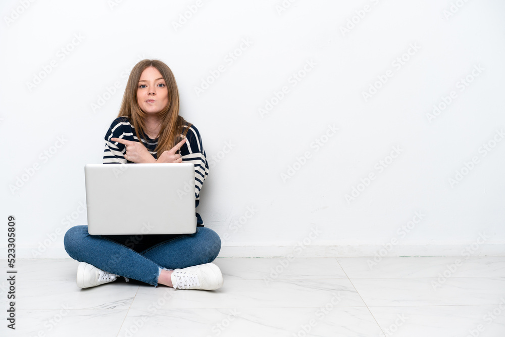 Young caucasian woman with a laptop sitting on the floor isolated on white background pointing to the laterals having doubts Young caucasian woman with a laptop sitting on the floor isolated on white background pointing to the laterals having doubts