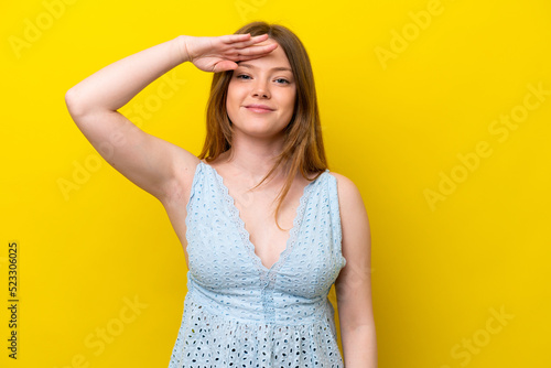 Young caucasian woman isolated on yellow background saluting with hand with happy expression