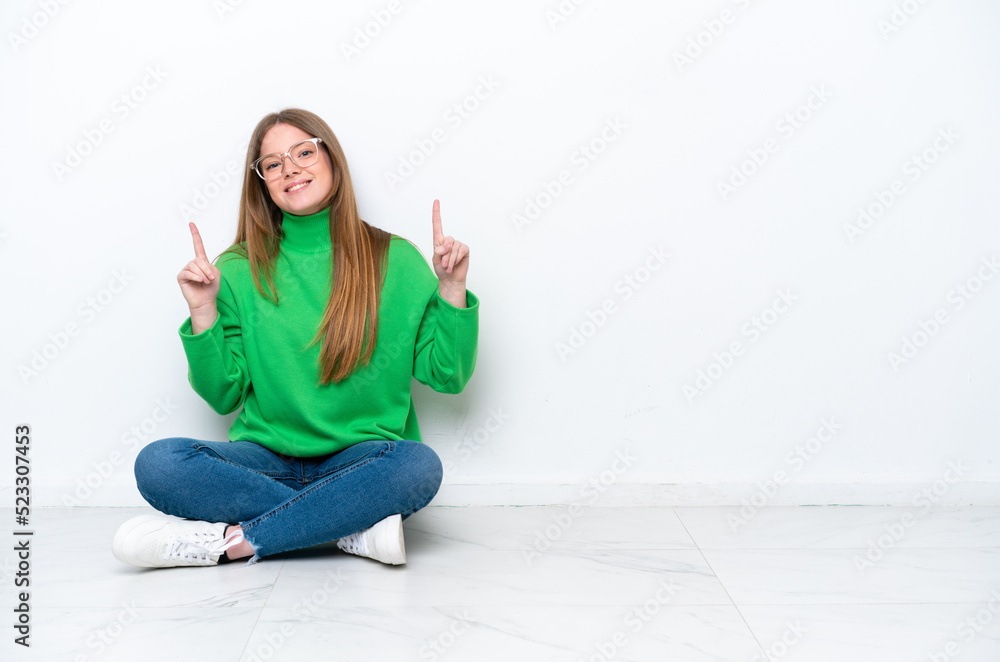 Young caucasian woman sitting on the floor isolated on white background pointing up a great idea