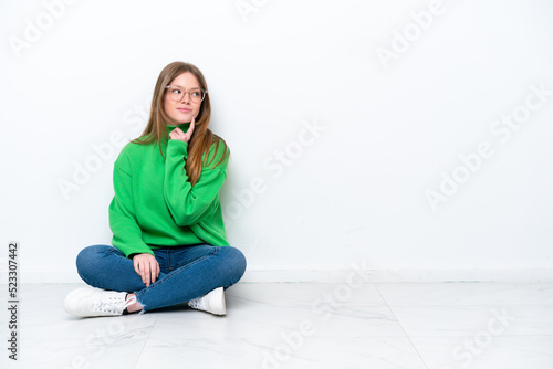 Young caucasian woman sitting on the floor isolated on white background thinking an idea while looking up