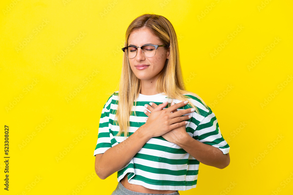 Blonde Uruguayan girl isolated on yellow background having a pain in the heart Blonde Uruguayan girl isolated on yellow background having a pain in the heart