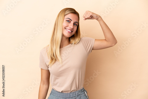 Blonde Uruguayan girl isolated on beige background doing strong gesture