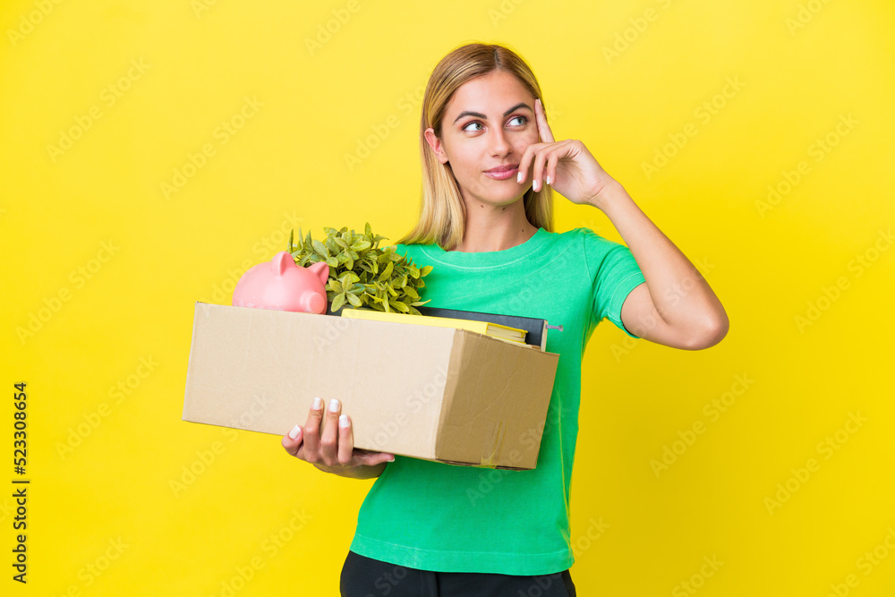 Young Uruguayan girl making a move while picking up a box full of things isolated on yellow background having doubts and thinking Young Uruguayan girl making a move while picking up a box full of things isolated on yellow background having doubts and thinking