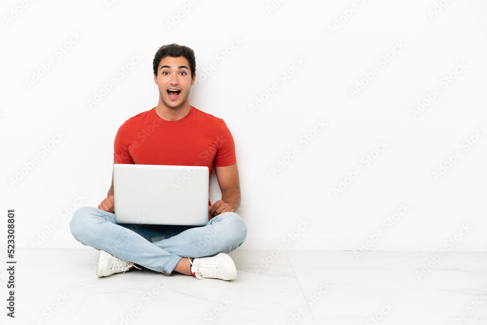 Caucasian handsome man with a laptop sitting on the floor with surprise facial expression Caucasian handsome man with a laptop sitting on the floor with surprise facial expression