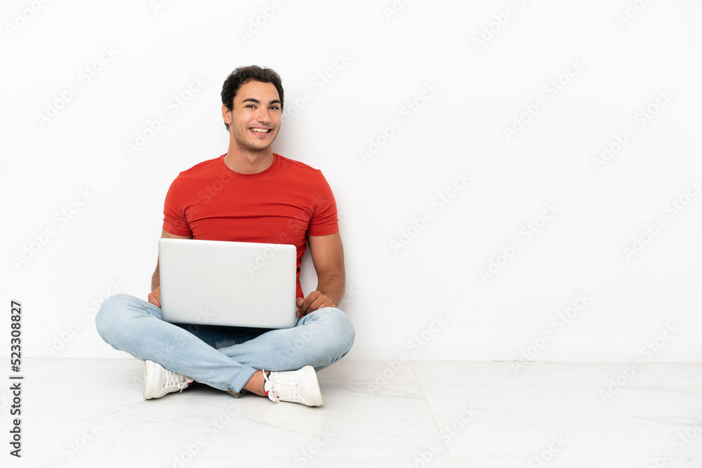 Caucasian handsome man with a laptop sitting on the floor with arms crossed and looking forward Caucasian handsome man with a laptop sitting on the floor with arms crossed and looking forward