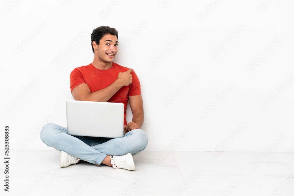 Caucasian handsome man with a laptop sitting on the floor pointing back Caucasian handsome man with a laptop sitting on the floor pointing back