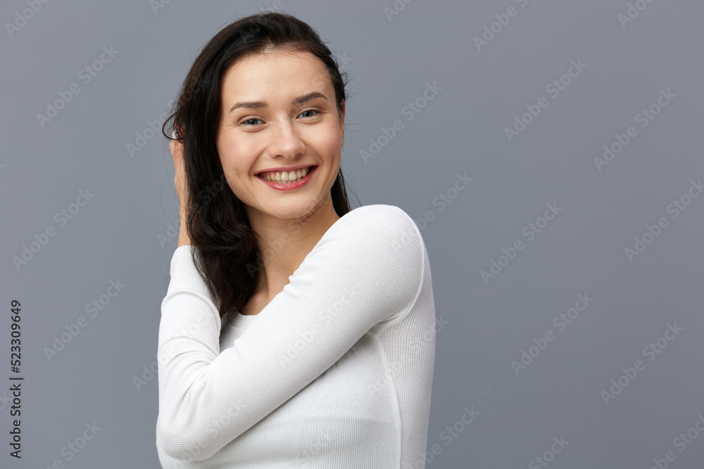 an excited woman stands on a gray background in a white T-shirt, squeezes her hair a little with her hand an excited woman stands on a gray background in a white T-shirt, squeezes her hair a little with her hand