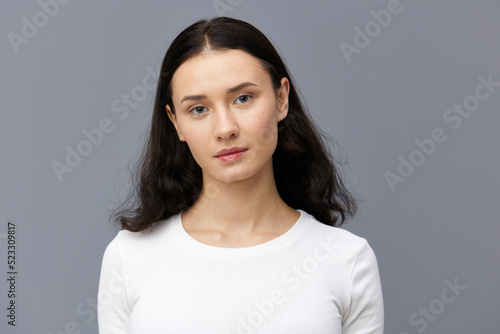 a gentle woman stands full-face on a dark background in a tight white T-shirt, calmly lowered her hands down and looks forward smiling sweetly