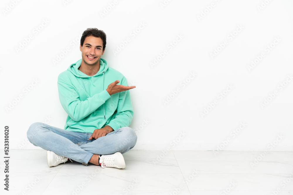 Caucasian handsome man sitting on the floor presenting an idea while looking smiling towards Caucasian handsome man sitting on the floor presenting an idea while looking smiling towards