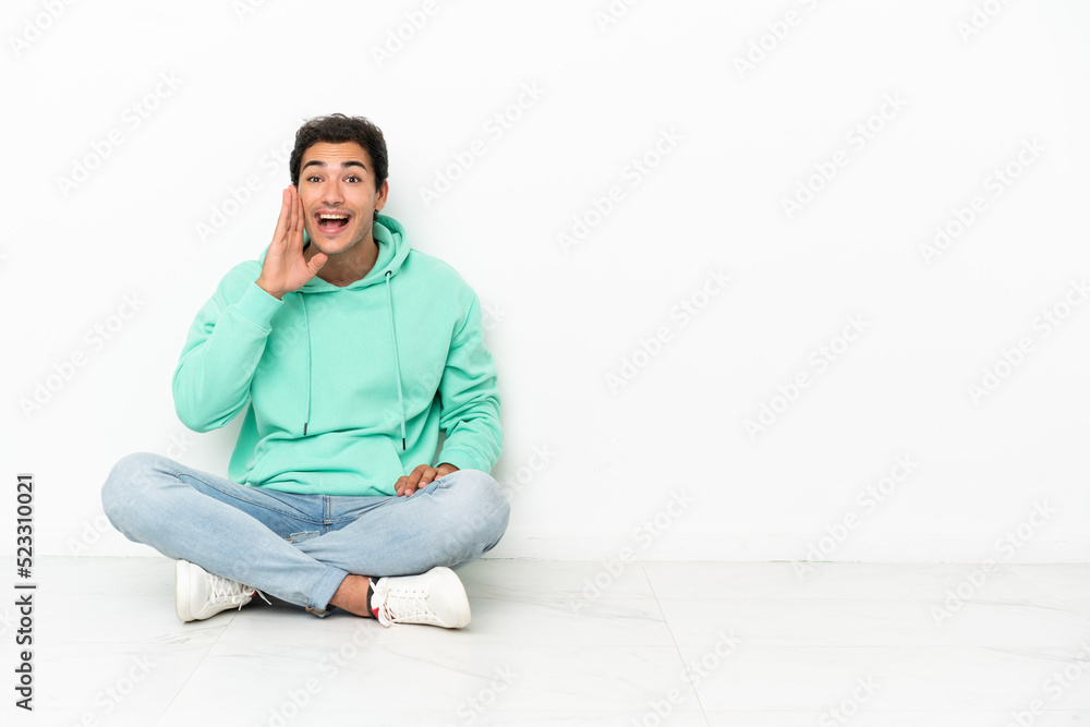 Caucasian handsome man sitting on the floor shouting with mouth wide open Caucasian handsome man sitting on the floor shouting with mouth wide open