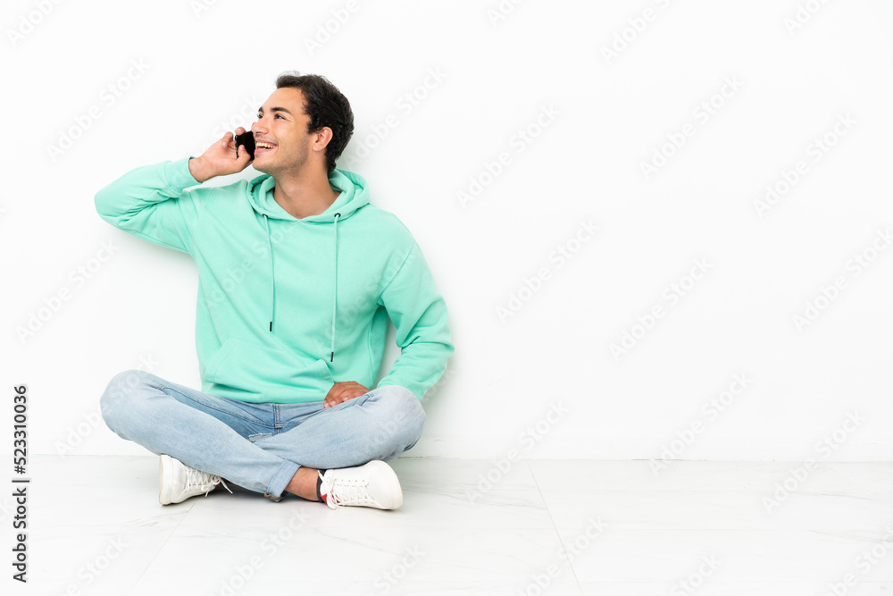 Caucasian handsome man sitting on the floor keeping a conversation with the mobile phone Caucasian handsome man sitting on the floor keeping a conversation with the mobile phone