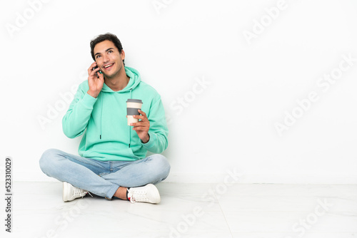 Caucasian handsome man sitting on the floor holding coffee to take away and a mobile