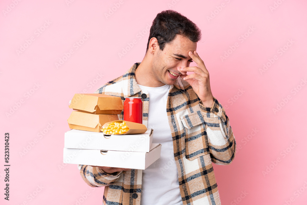 Young caucasian man holding fast food isolated on pink background laughing Young caucasian man holding fast food isolated on pink background laughing