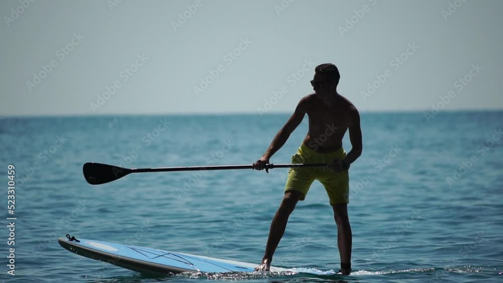 Sea man sup. Athlete man swimming in sea and paddleboarding at summer sunset. Healthy strong male enjoy outdoor active lifestyle and water sports on holiday vacation. Slow motion Sea man sup. Athlete man swimming in sea and paddleboarding at summer sunset. Healthy strong male enjoy outdoor active lifestyle and water sports on holiday vacation. Slow motion