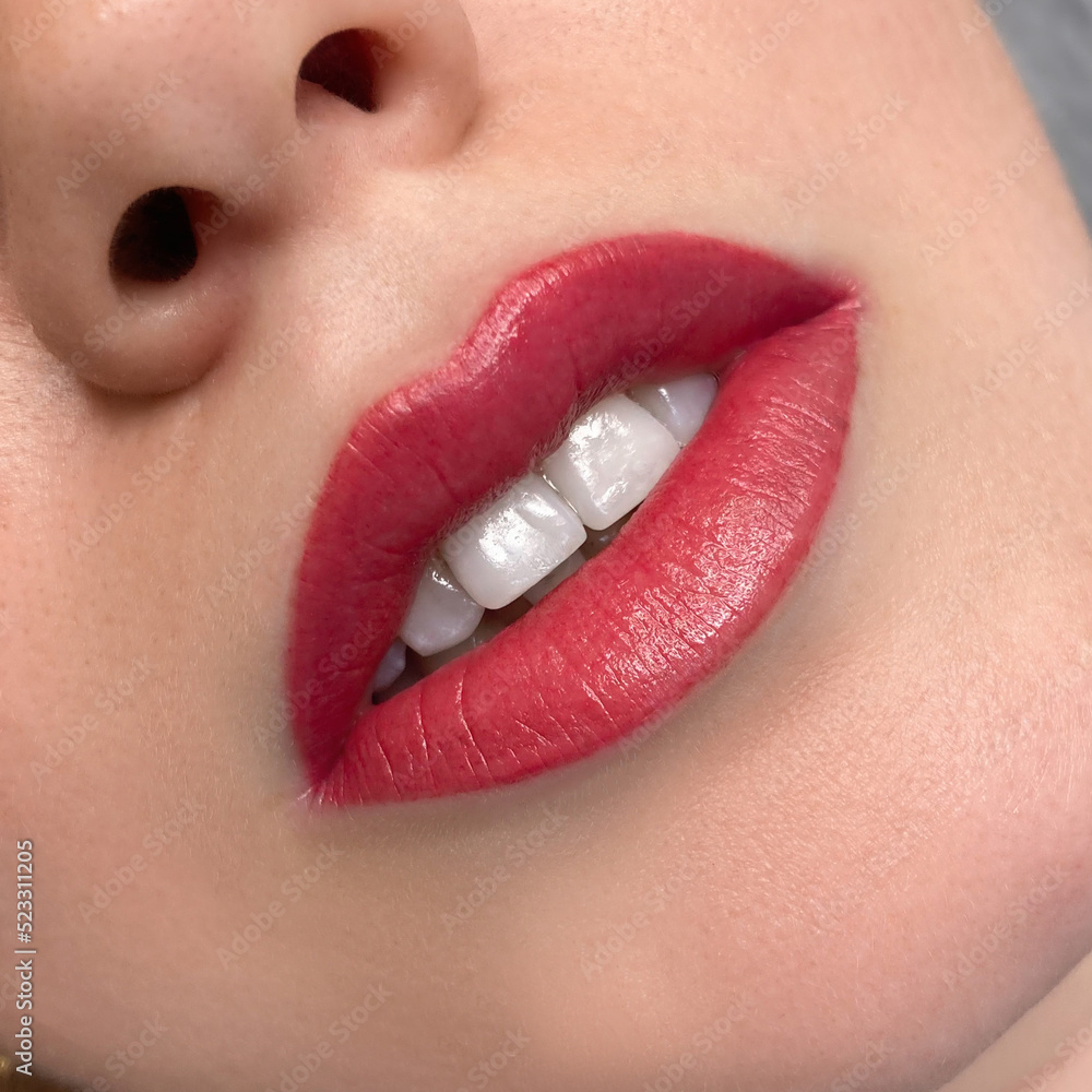 Fototapeta premium permanent makeup on the lips of a young woman of a delicate peach shade close-up, a girl after a cosmetic procedure with smooth and clean healthy skin, womans white teeth