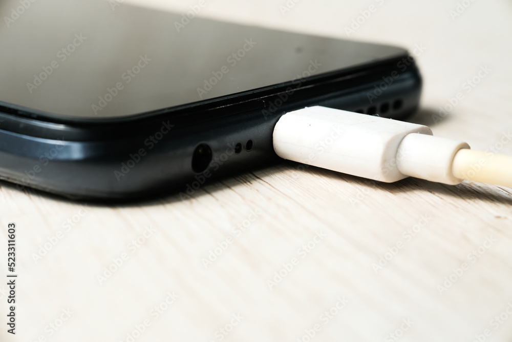 Modern smartphone charging on wooden table. Modern technology concept. Selective focus Modern smartphone charging on wooden table. Modern technology concept. Selective focus