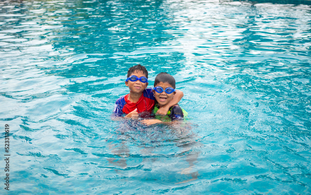 Brothers wear a swimsuit and goggles. Smile and enjoy playing in the water in the blue pool