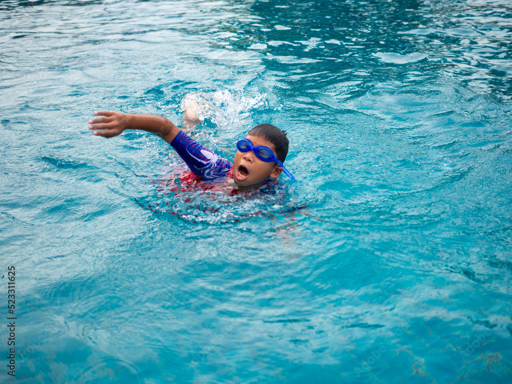 boy wearing a swimsuit and glasses swimming in the middle of the pool with a blue water background