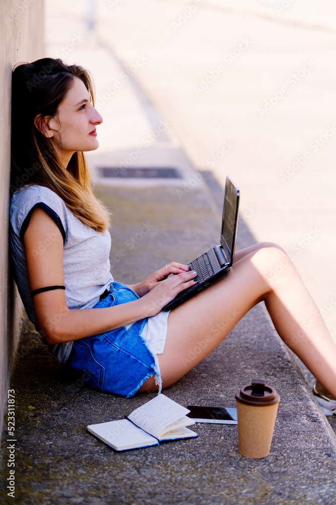 Blonde girl sitting on the floor working with the laptop.