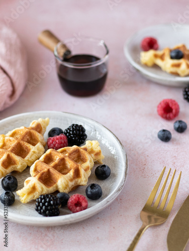 Croffles (combination of croissant and waffle) with fresh raspberry, blueberry and blackberry served in ceramic plate on pink table. Kitchen towel on background. Food trend from South Asia. Close up photo