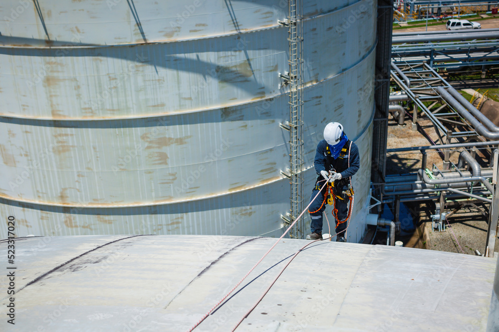 Male worker inspection wearing safety first harness rope safety line working at a high place on tank roof spherical gas  blue sky