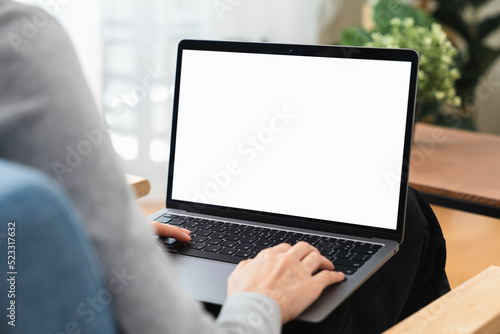 Woman hand using laptop and typing on keyboard with mockup of blank screen on wooden table.