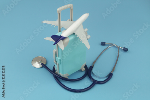 Airplane on suitcase and stethoscope on blue background. Travel insurance, medical tourism, health care concept.