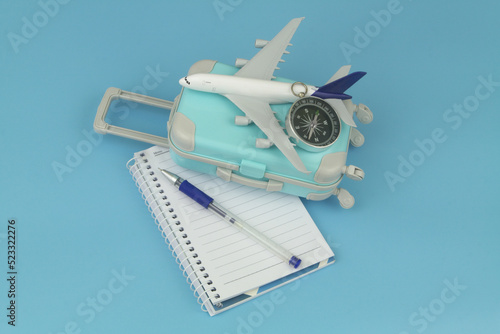Counting travel budget and planning travel directions concept. Airplane with compass on suitcase and notebook with pen.