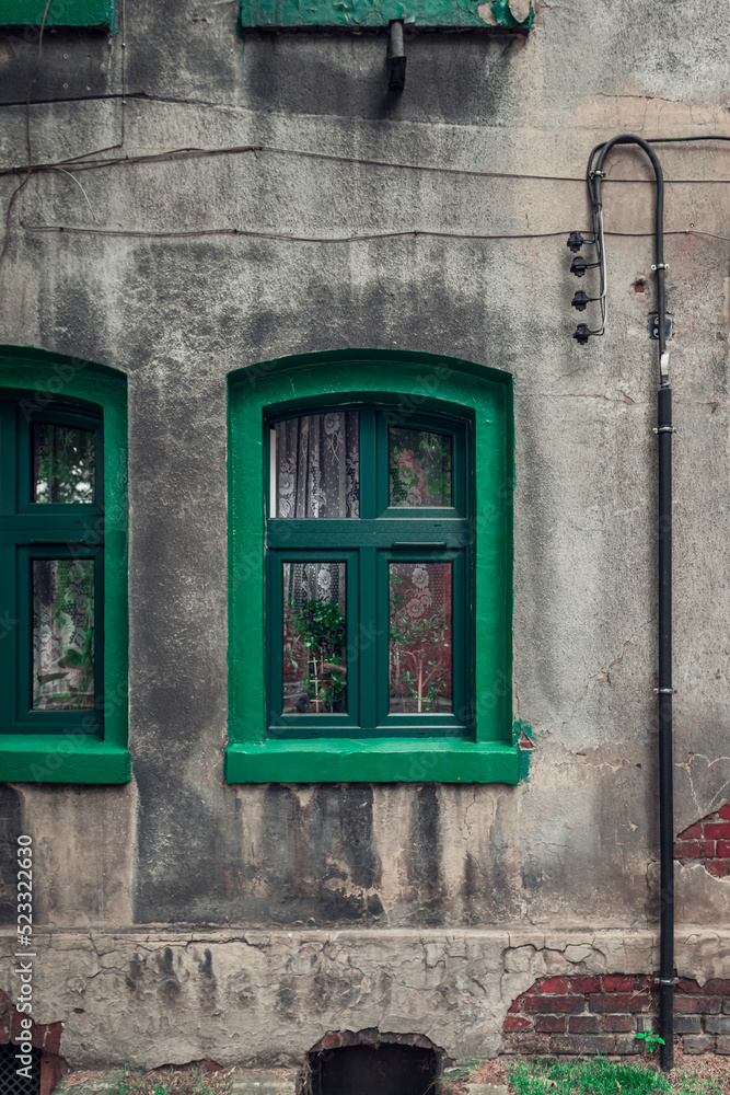 A green window with a green window sill against the background of a gray, plastered, damaged wall