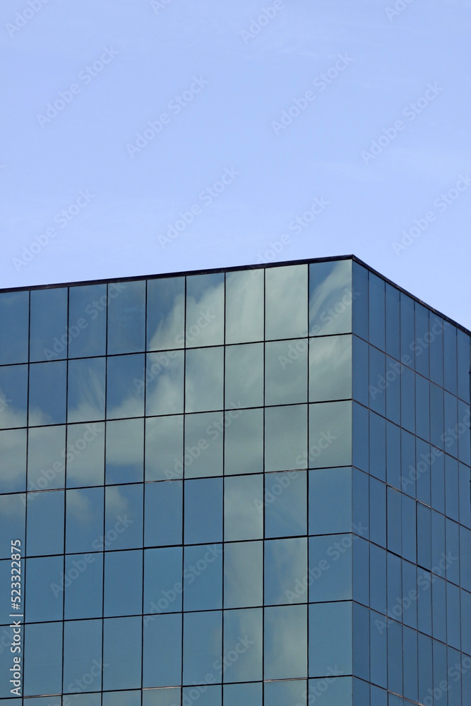 Clouds reflect in the windows of a generic modern office building's facade with clear blue sky in the background