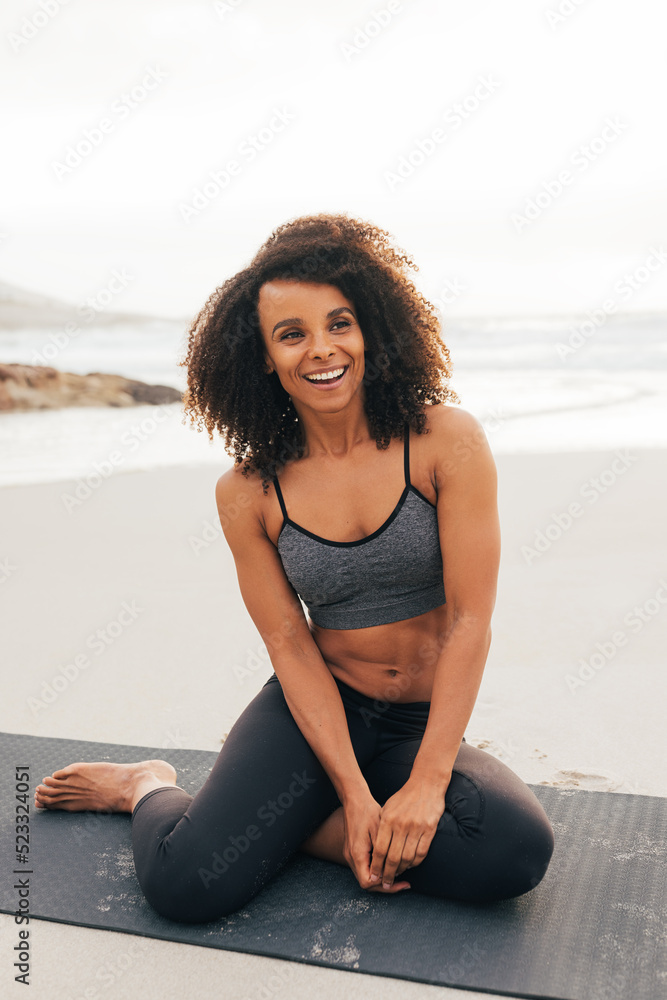 Happy woman with curly hair sitting on mat at beach. Smiling female relaxing after yoga exercises. Happy woman with curly hair sitting on mat at beach. Smiling female relaxing after yoga exercises.