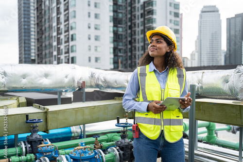 Service engineer woman dark skin wearing uniform and safety helmet under inspection and checking production process,HVAC system (Heating,Ventilation and Air Conditioning) on factory station by tablet. photo