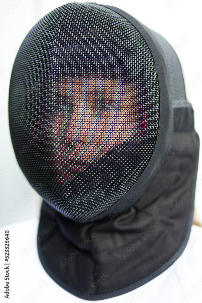 Closeup of black metal mask (helmet) on female head for electric and non-electric sabre fencing on white background. Weapon safety, protective gear. Vertical plane. Closeup of black metal mask (helmet) on female head for electric and non-electric sabre fencing on white background. Weapon safety, protective gear. Vertical plane.